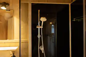 Duschkopf und Armatur in einer Camping-Badezimmertür, mit beleuchteten Wänden und Fliesen im Hintergrund.
