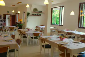 Speisebereich im Camping-Restaurant mit gedeckten Tischen, Holzstühlen, warmen Lampen und Blick durch große Fenster.