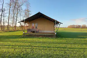 Mobilheim mit Veranda auf grünem Rasen, Holzstufen und Geländer, im Hintergrund Bäume und freies Feld.