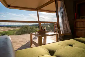 Innenansicht eines Wohnwagens mit gruenen Polstern, Blick auf die Terrasse und das Landschaftspanorama durch geoeffnete Tuer.
