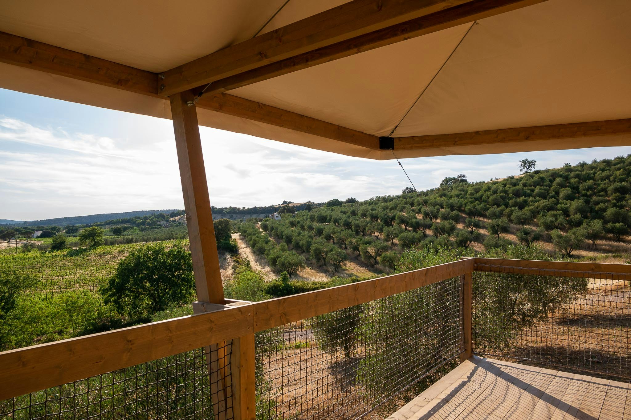 Balkon mit Holzgeländer und Sicht auf grüne Hügel und Felder, vom überdachten Campingbereich aus.