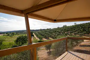 Balkon mit Holzgeländer und Sicht auf grüne Hügel und Felder, vom überdachten Campingbereich aus.
