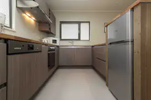 Moderne Küchenzeile mit Herd und Spüle, Kühlschrank und Fenster im hellen Wohnbereich eines Camping-Mobilheims.