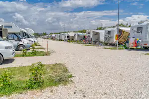 Wohnmobile auf einem Campingplatz mit Kiesweg, Stellplätzen und Fahrrädern neben den Fahrzeugen.