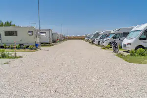 Wohnmobile und Camper stehen auf einem Schotterweg, links und rechts mit Büschen und Laternen im Campingplatzbereich.