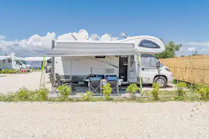 Wohnmobil mit Markise und Sitzbereich auf einem Stellplatz, daneben weitere Fahrzeuge und Wohnmobile im Campingbereich.