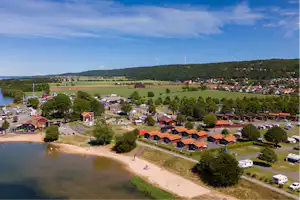Luftaufnahme eines Campingplatzes am See mit Uferpromenade, Stellplätzen, Wohnwagen und Häusern am Hang.