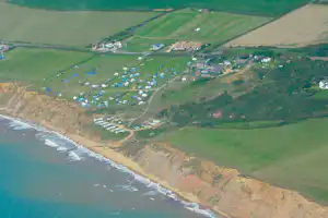 Luftaufnahme eines Campingplatzes an der Küste mit Strand, Wohnwagen und Zelten in grünen Feldern und Wegen.