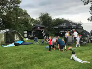 Campingplatz im Grünen: Zelte, Vorzelt und Campingstühle, Kinder und Erwachsene stehen auf dem Rasen.