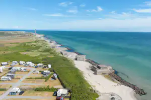 Campingplatz mit Wohnwagen und Stellplätzen am Küstenweg, Blick auf das Meer und den Strandabschnitt mit Wellenbrechern.
