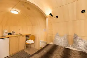 Innenansicht eines Camping-Unterkunftsraums mit Küchenzeile, zwei Sitzkissen und kleinem Tisch, warmem Licht und Fliesenboden.