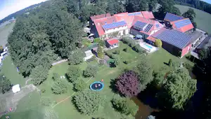 Campinganlage mit mehreren Gebäuden und roten Dächern, umgeben von Bäumen und Grünflächen, mit kleinem Rundbecken im Garten.