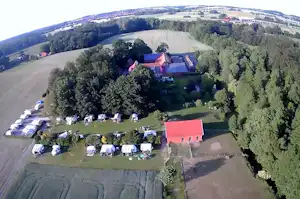 Luftaufnahme eines Campingplatzes mit Wohnwagen und Zelten, umgeben von Wiesen, Feldern und Wäldern in einem Tal.