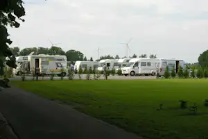 Wohnwagen und Campingbusse stehen auf einer grünen Campingwiese, mit Hecken und Bäumen am Rand des Stellplatzes.