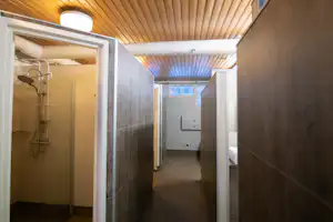 Flur mit Holzdecke und Dusche im Sanitärbereich eines Campingplatzes, mit Duschkopf und Tür zum Nebenraum.