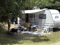 Happy Camping - Gäste vor ihrem Wohnmobil im Schatten  auf dem Campingplatz
