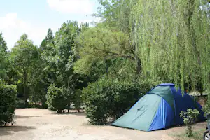 Campingzelt am Rand eines Kieswegs im Grünen, umgeben von Bäumen und Sträuchern.