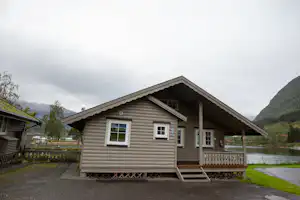 Ein Mobilheim auf einem Campingplatz mit Holzveranda, Treppe und Blick auf Berge im Hintergrund.