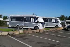 Wohnmobil auf dem Stellplatz mit Tisch und Stühlen vor dem Fahrzeug, Hecken und Steinumrandung am Rand.
