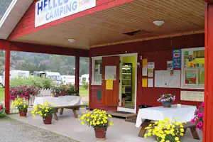 Rezeption am Campingplatz mit Holzüberdachung, Sitzbänken und Tischen sowie Blumenampeln vor dem Eingang.
