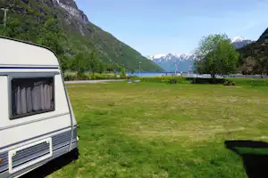 Wohnwagen am Campingplatz auf grünem Rasen, Blick auf den Fluss und Berge im Hintergrund.