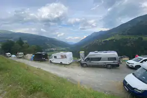 Wohnmobile und Autos auf einem Campingplatz am Hang, im Hintergrund grüne Berge und ein Tal.