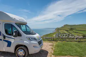 Wohnmobil am Campingplatz mit Meerblick, Grasfläche und Holzgeländer, im Hintergrund Küste und grüne Hügel.