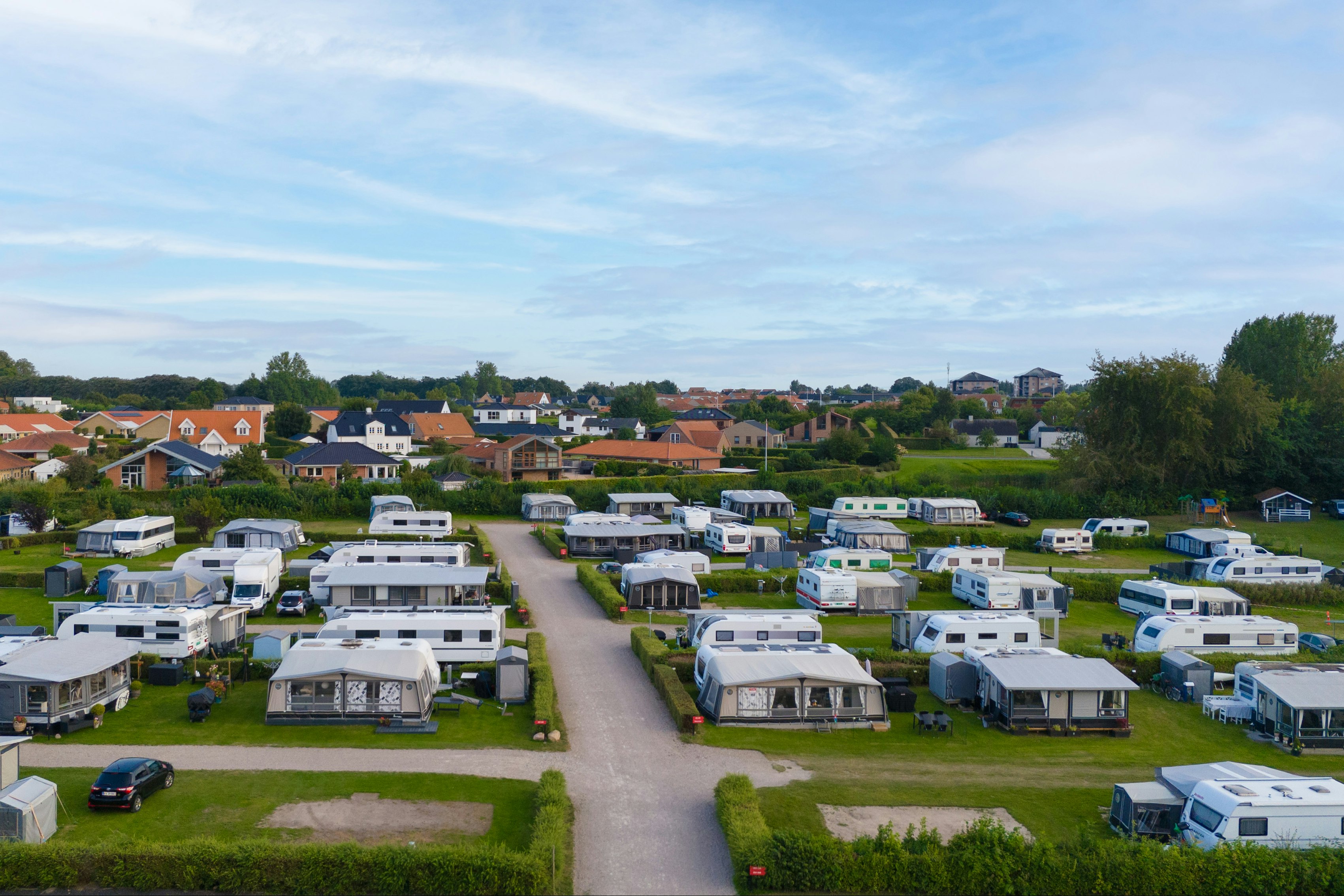Campingplatz mit vielen Wohnwagen und Mobilheimen, gepflegten Rasenparzellen und einem breiten Weg zwischen den Stellplätzen.