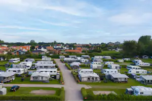 Campingplatz mit vielen Wohnwagen und Mobilheimen, gepflegten Rasenparzellen und einem breiten Weg zwischen den Stellplätzen.