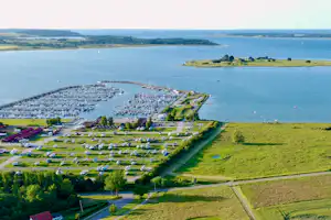 Luftaufnahme einer Küstenlandschaft mit Bucht, grünen Wiesen, Wegen und einem kleinen Ort am Wasser.