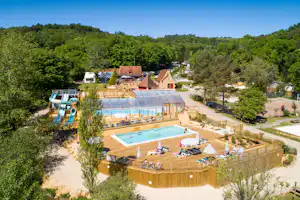 Campinganlage mit Pool, Sonnenschirmen und Liegestühlen, überdachtem Bereich sowie Wasserrutsche, umgeben von Bäumen und Wegen.