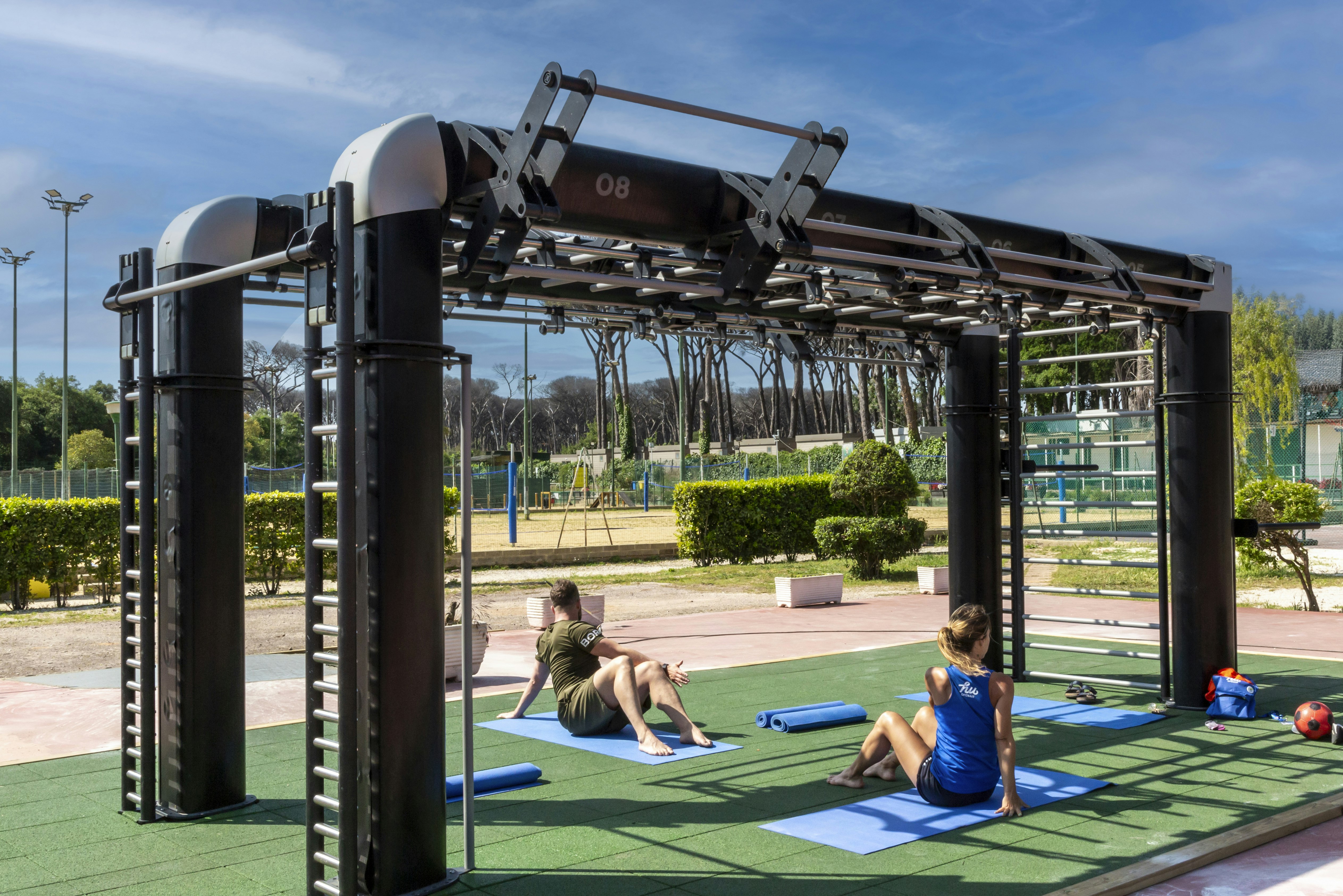 Sportbereich auf dem Campingplatz: Kinder spielen auf dem grünen Kunstrasen, im Vordergrund ein Kletter- und Turngerüst.