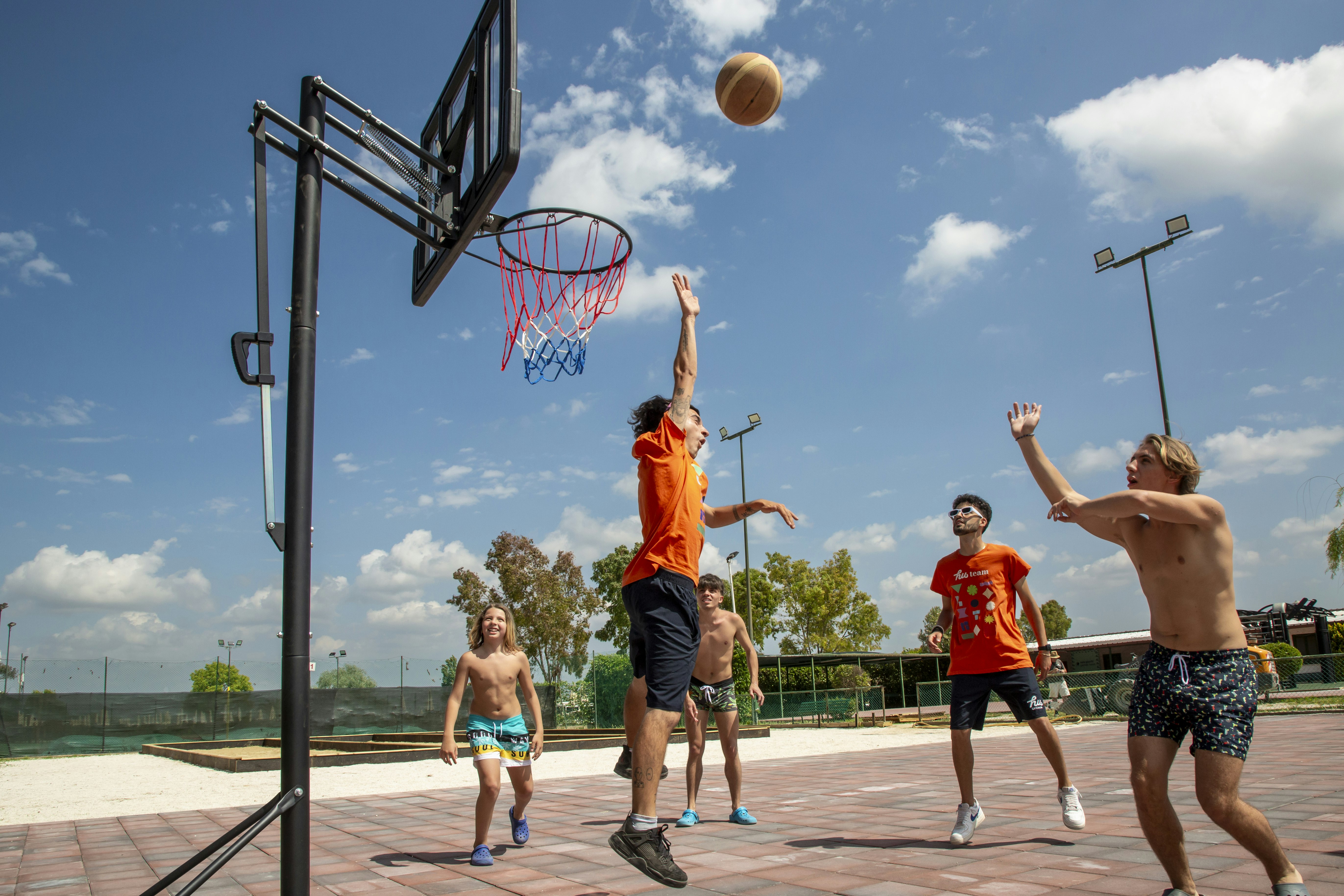 Basketballkorb auf einem Campingplatz, Kinder spielen Basketball auf dem gepflasterten Platz vor blauem Himmel.