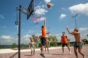 Basketballkorb auf einem Campingplatz, Kinder spielen Basketball auf dem gepflasterten Platz vor blauem Himmel.