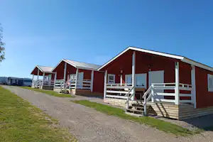 Rote Ferienhäuser mit Veranda und Treppen, Kiesweg und Rasen am Campingplatz, im Hintergrund weitere Bungalows.