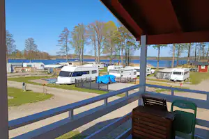 Blick vom Balkon auf einen Campingplatz mit Wohnwagen, Stellplätzen, Wegen und Bäumen am Rand.