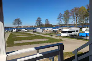 Campingplatz mit Stellplätzen, Wohnwagen und Wohnmobilen, Rasenflächen und Wegen, im Hintergrund ein See und Bäume.