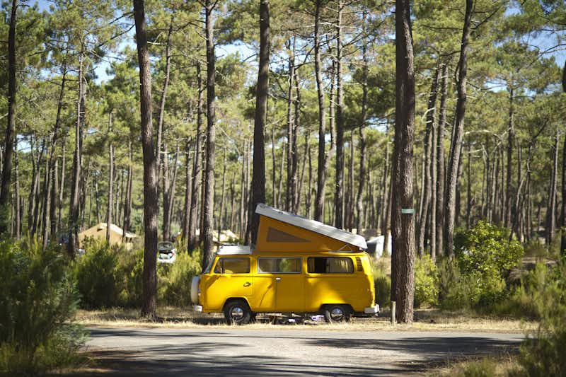 Huttopia Camping Lac de Carcans - Gelbes Wohnmobil auf dem Stellplatz zwischen den Bäumen auf dem Campingplatz