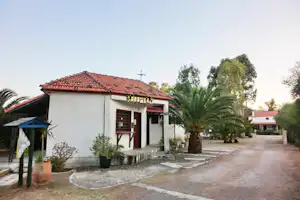 Campinghaus mit rotem Ziegeldach, Eingangstür und Veranda, daneben Palmen und ein gepflasterter Weg im Hof.