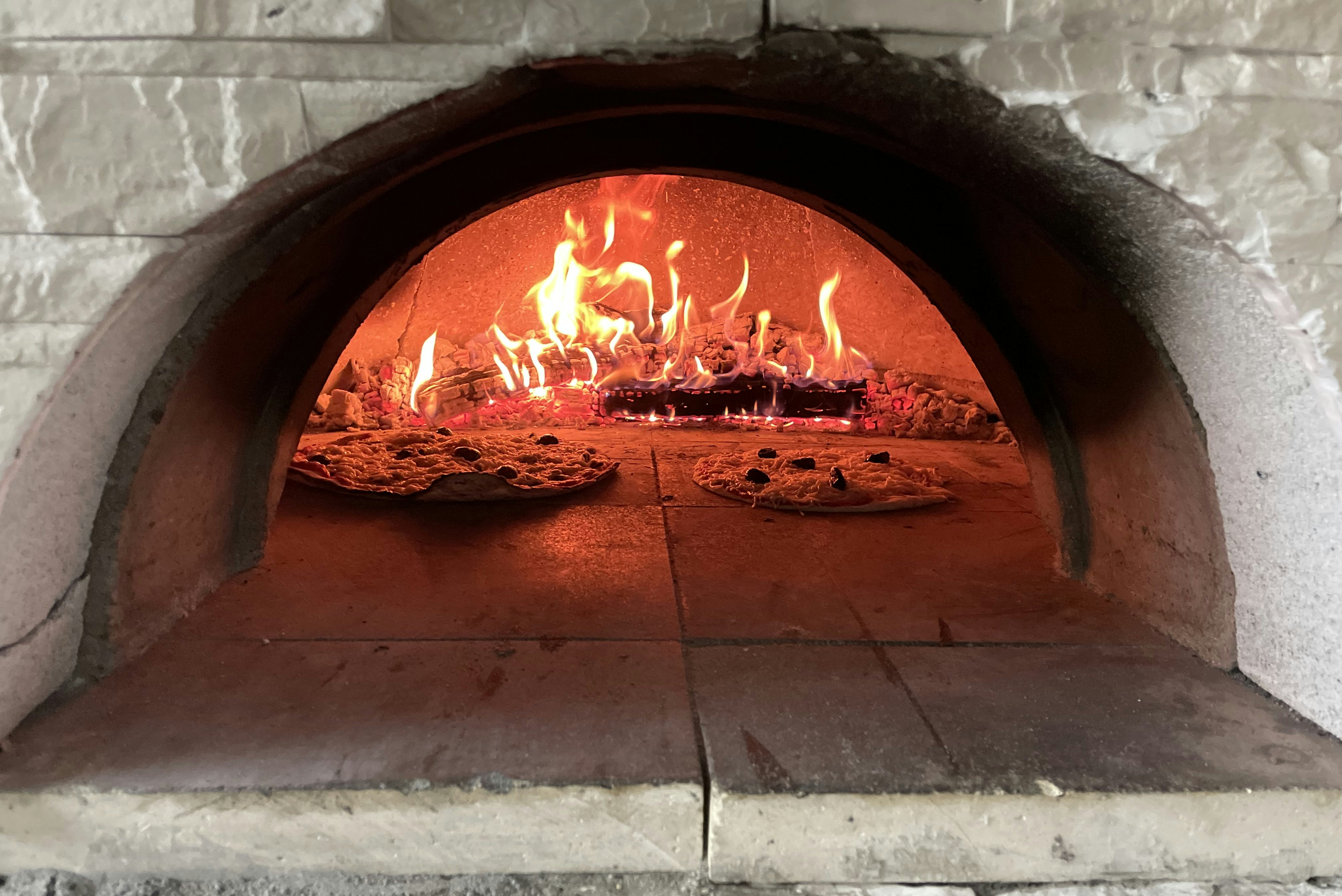 Flammen im Steinofen mit Feuerstelle, Ziegelboden und zwei Pizzablechen im Vordergrund.