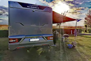 Wohnmobil am Campingplatz mit Vorzelt, Stühlen und Tisch auf dem Stellplatz, im Hintergrund Wiese und Bäume.