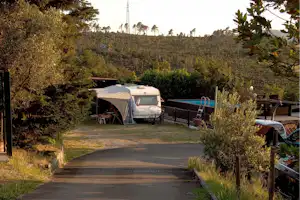 Wohnwagen auf einem Campingplatz-Stellplatz mit Vorzelt, Tisch und Stühlen, umgeben von Büschen und Bäumen.
