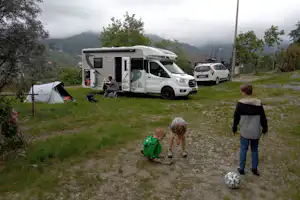 Wohnmobil auf dem Campingplatz mit Vorzelt, daneben Auto und Zelt, im Hintergrund Bäume und Berge im Nebel.