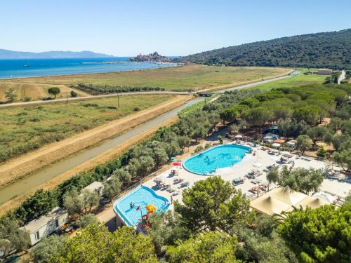 Campinganlage mit zwei Pools, Liegen und Zelten am Rand eines grünen Hangs, Blick auf das Meer und die Bucht.