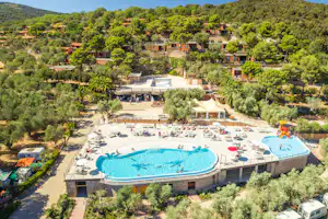 Blick auf den Campingpool mit Liegen, Sonnenschirmen und einem großen Becken, umgeben von Bäumen und Ferienhäusern.
