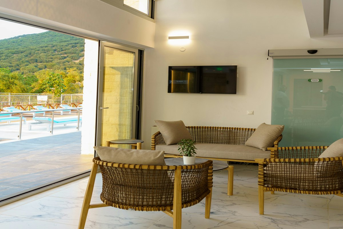 Terrasse mit Lounge-Sitzgruppe und Couchtisch vor großen Schiebetüren, Blick auf grüne Hügel und mehrere Sonnenliegen.