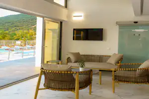 Terrasse mit Lounge-Sitzgruppe und Couchtisch vor großen Schiebetüren, Blick auf grüne Hügel und mehrere Sonnenliegen.