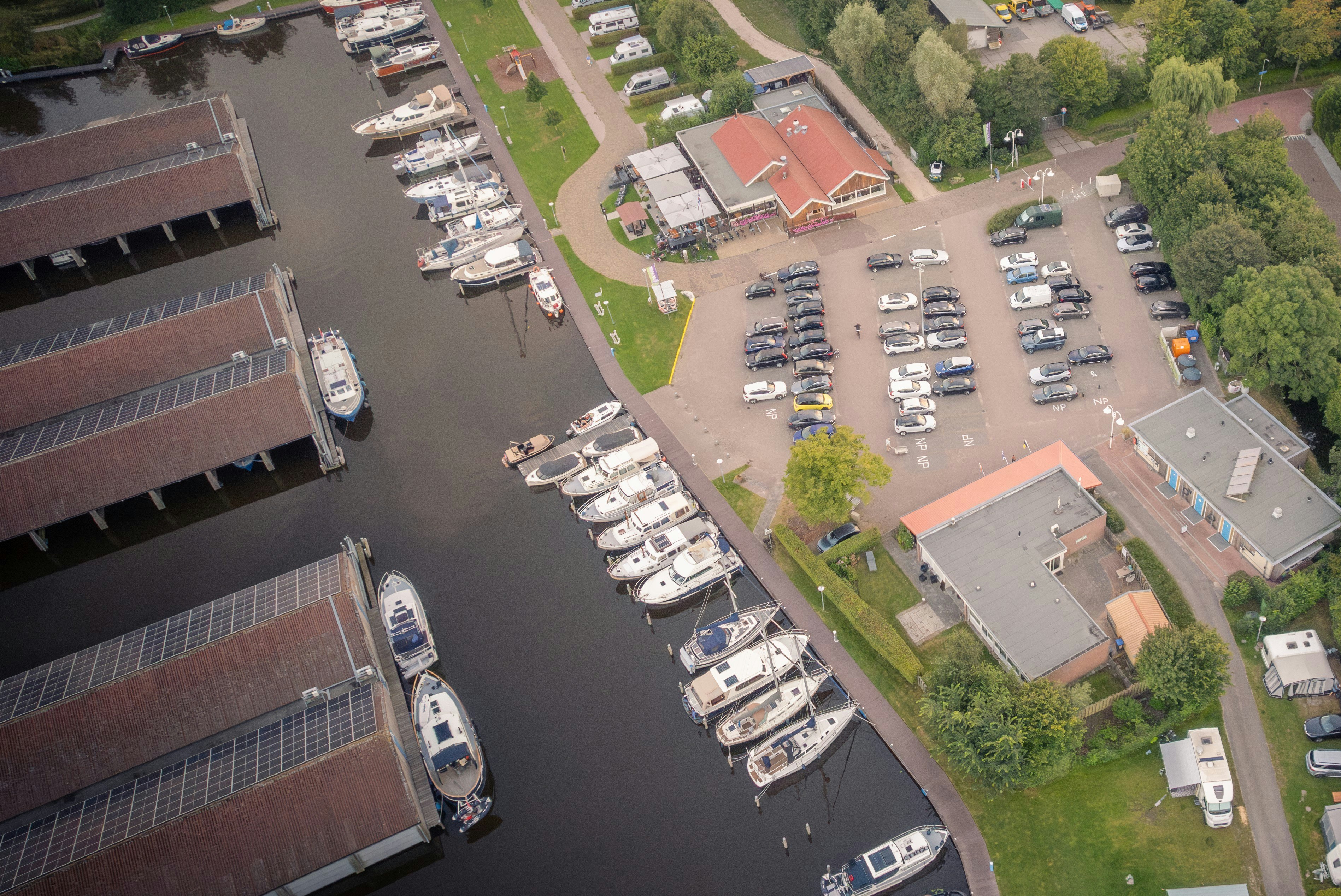 Luftaufnahme eines Campingplatzes am Fluss mit Bootsstegen, Stellplätzen, Wohnmobilen und mehreren Gebäuden im Grünen.