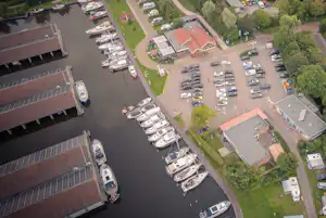 Luftaufnahme eines Campingplatzes am Fluss mit Bootsstegen, Stellplätzen, Wohnmobilen und mehreren Gebäuden im Grünen.