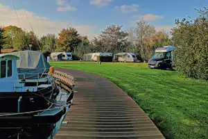 Wohnwagen und Zelte auf einem Campingplatz, mit breitem Holzweg durch das grüne Gras und weiteren Fahrzeugen im Hintergrund.